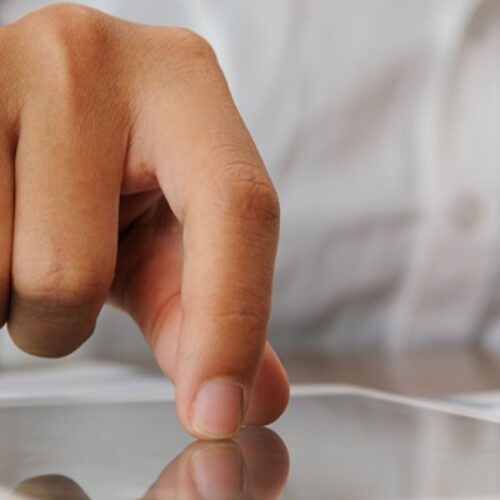 Closeup of person tapping on touchscreen. Tablet and papers lying on desk. Technology and paperwork concept. Cropped view.