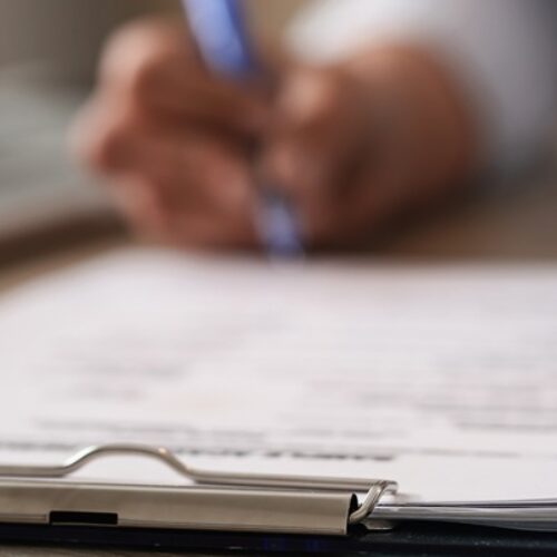 Close up of unrecognizable business person signing documents in the office.
