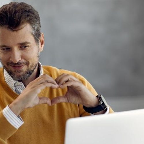 Smiling businessman showing a heart shape while having video call over laptop in the office.