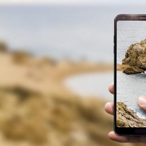A closeup of a hand holding a phone taking a photo of a beach